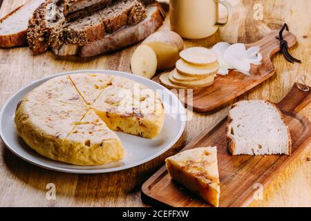 Fresh cut pie on ceramic plate placed on wooden table with cutting boards with pieces of pie, bread and sliced vegetables Stock Photo