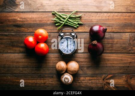 Assorted fresh vegetables and bottle of oil lying on timber tabletop near various cooking tools Stock Photo