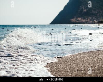Coast line by sea in storm. Blue sea water and waves with white foam line on coast. Stock Photo