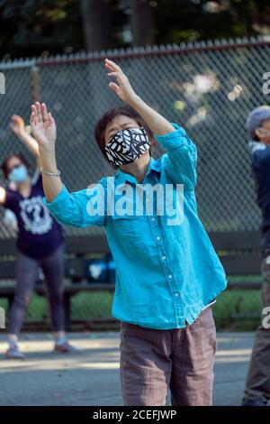 A middle aged Asian American woman wearing a face mask attends a Tai Chi class in Kissena Park, Flushing, Queens, New York City Stock Photo