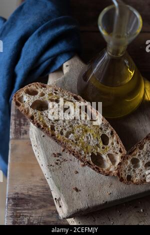 From above shot of slices of yummy wholemeal bread of kamut and spelt with beer complemented with oil lying wooden cutting board near towel Stock Photo