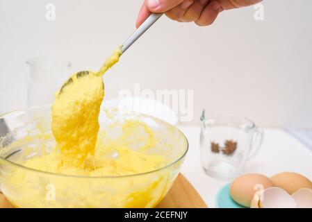 the dough for cupcakes made of rice flour, butter, eggs, sugar runs off the spoon. close-up of the dough texture in a transparent dish. Stock Photo