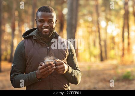 Positive african man drinking tea at forest Stock Photo