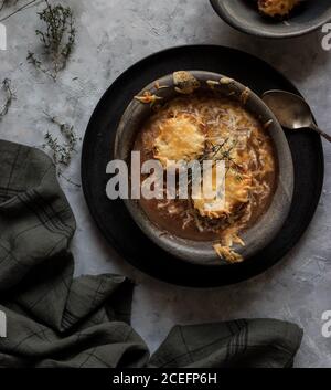 Metal bowl with palatable French onion soup standing near towel on gray plaster surface Stock Photo