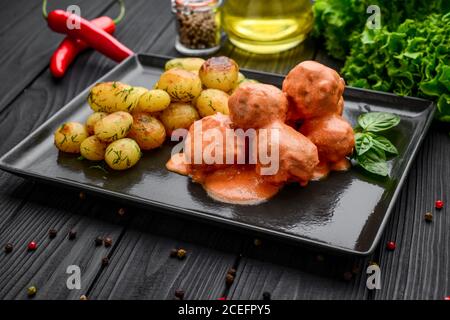 Meatballs in tomato, with boiled potatoes on a black plate Stock Photo