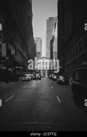 Black and white shot of parked and driving cars on street between skyscrapers in New York. Stock Photo