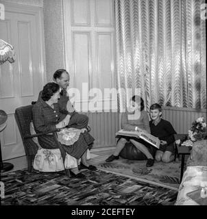 A Scottish couple relax in their living room with their two young children, kept warm by their new coal fired central heating system, in the 1950s Stock Photo