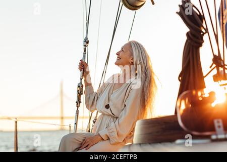 Side view of mature woman with long hair sitting on yacht and smiling Stock Photo