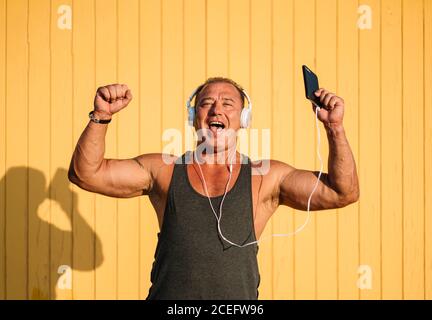 Strong older man poses with headphones on yellow background. Stock Photo