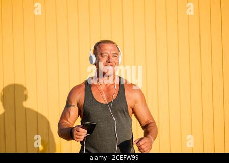 Strong older man poses with headphones on yellow background. Stock Photo