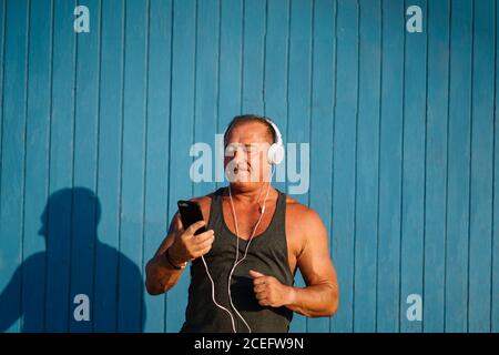 Strong older man poses with headphones on blue background. Stock Photo