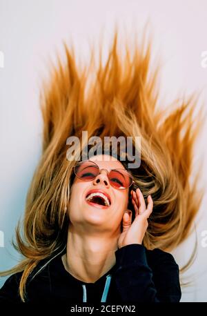 Young blond Woman in black pullover and sunglasses with long hair dancing in studio and smiling on white background Stock Photo