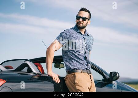 Handsome Stylish Man In Sunglasses Posing Near Car And Looking At Camera  Stock Photo, Picture and Royalty Free Image. Image 128145889.