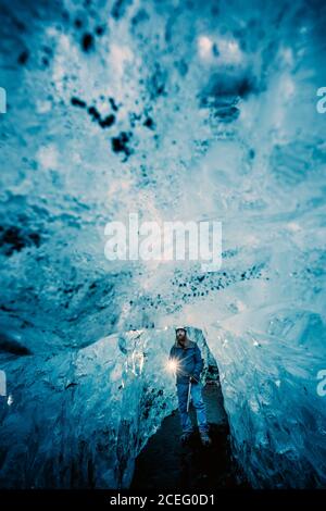 Traveler with burning torch standing in hall of crystal blue ice cave, Iceland Stock Photo