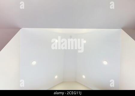 suspended ceiling with halogen spots lamps and drywall construction in empty room in apartment or house. Stretch ceiling white and complex shape. Stock Photo
