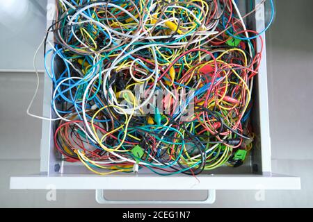 Disorganized colorful cables on a drawer. Messy wires. Stock Photo