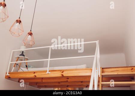 Interior of bedroom with wooden stairs and bed on second floor with bedside table, pendant light hanging on ceiling Stock Photo