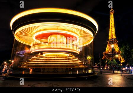 Bright traces of light on spinning carousel near magnificent Eiffel Tower at night in Paris, France. Stock Photo