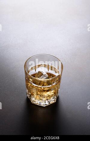 One shot of whiskey with ice cube on dark brown background. Stock Photo