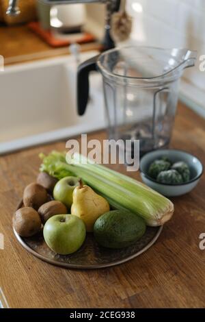 Composed fresh green vegetables and fruit on plate placed on top of wooden counter in kitchen Stock Photo