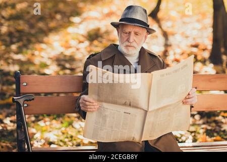 Photo of focused old man grandfather sit bench autumn town park read interesting bought newspaper wear cap headwear Stock Photo