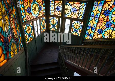 Elegant colorful stained-glass panel on vintage staircase in old shabby wooden building in daylight Stock Photo