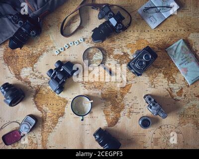 Mug of fresh coffee and assorted tourist stuff lying on retro world map