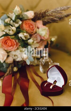 Wedding bridal bouquet of roses and eucalyptus branches next to a box of wedding rings on yellow velvet. Wedding and love concept. Stock Photo