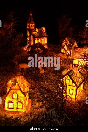 Homemade Christmas decoration from lit tiny ceramic houses. Realistic Xmas model of miniature Nativity scene in rural night village. Christian church. Stock Photo