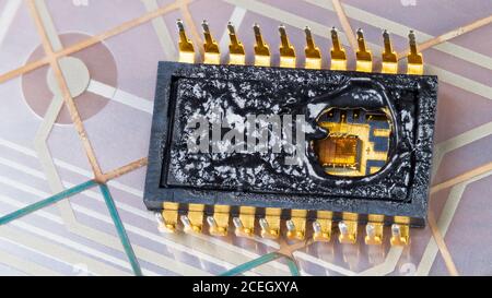 Inside of burned integrated circuit on flexible PCB membrane detail. Visible silicon wafer and fine gold wires in hole of molten microchip DIP package. Stock Photo
