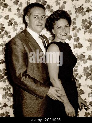 Happy posed couple circa 1960s dressed up in fashionable evening clothing, woman holding cigarette. Stock Photo