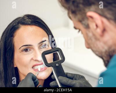 unrecognizable dentist looking through magnifying glass and trying denture dye sample for Woman Stock Photo