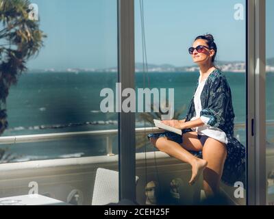 Attractive young Woman leaning on handrail and relaxing with book at the seaside. Stock Photo