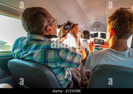 A passenger photographs the landscape and light through the cockpit window during a scenic flight over northern Australia, while the passenger beside him captures the scene on a smartphone. Stock Photo