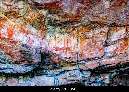 Several red hand stencils are painted on the rock wall of a shelter near Point Stuart, Northern Territory, Australia – an Aboriginal rock painting seen on Sab Lord's guided tour. Stock Photo