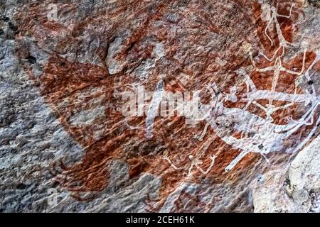 White, dance-like stick figures are painted over an older red ochre surface, photographed on a rock overhang near Mount Borradaile, Northern Territory, Australia. Stock Photo