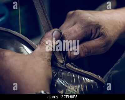 Closeup dirty hands of shoemaker cutting leather from shoes while working in workshop Stock Photo