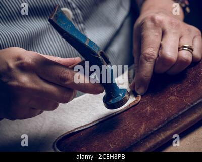 Closeup anonymous man using hammer while working with piece of leather in workshop Stock Photo