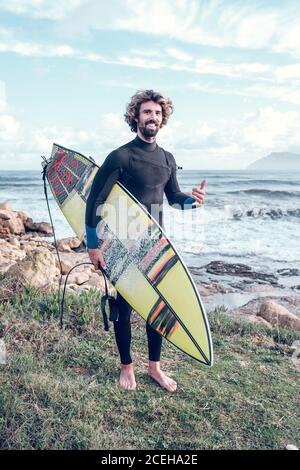 Young man in wetsuit with surf board near sea Stock Photo