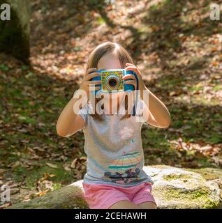 Morgantown, WV - 20 August 2020: Small caucasian girl in a forest taking photo using Vtech Digizoon digital camera in forest Stock Photo