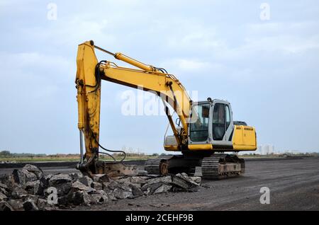 Large tracked excavator with hydraulic hammer breaks asphalt at a construction site on the background sunset. Breaking rock and reinforced Concrete. R Stock Photo