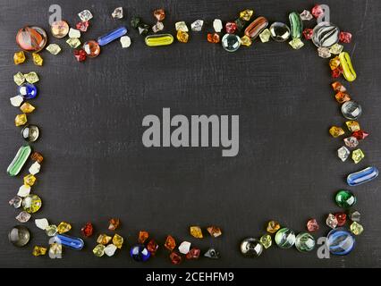 Multicolored glass marble balls and glass pebbles on black surface in frame shape. Colored stones of Mancala game on board Stock Photo