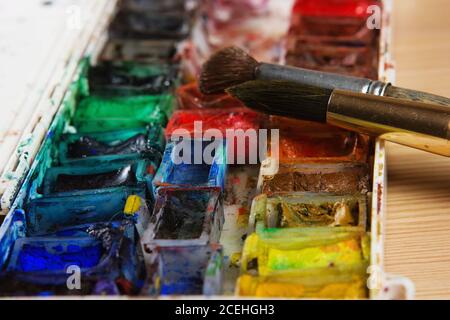 artists brushes and watercolour paints on palette. Vintage stylized photo of paintbrushes closeup and artist palette. Used palette with paintbrush Stock Photo