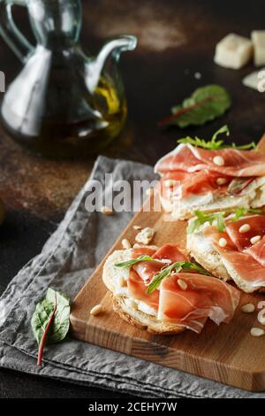 Traditional parma cured ham antipasto. Bruschetta set with Parma Ham and Parmesan Cheese. Small sandwiches with prosciutto, parmesan cheese, fresh aru Stock Photo