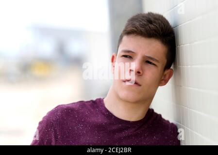 Close up portrait of a young teenager leaning on a wall while looking away Stock Photo