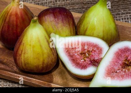 Fresh fig sliced in half with whole figs in the background, on a wooden surface. Fig fruits on a wooden platter. Stock Photo