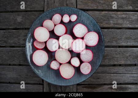 red radish slices on a blue plate on a wooden table Stock Photo