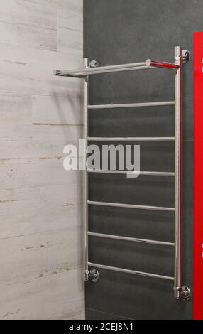Modern chrome heated towel rail hanging on gray ceramic tiled in the bathroom wall. Luxury light themed background for interior and design. Small shar Stock Photo