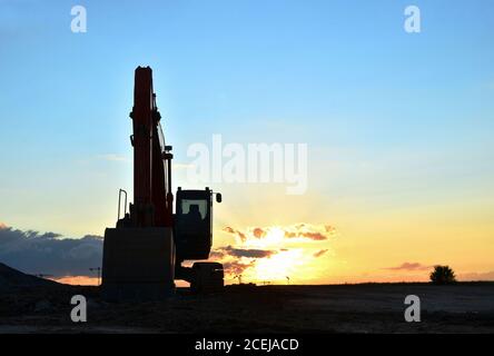 Large tracked excavator on a construction site against the background of the awesome sunset. Road repair, asphalt replacement. Small roughness sharpne Stock Photo