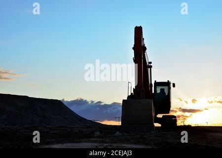 Large tracked excavator on a construction site against the background of the awesome sunset. Road repair, asphalt replacement. Small roughness sharpne Stock Photo